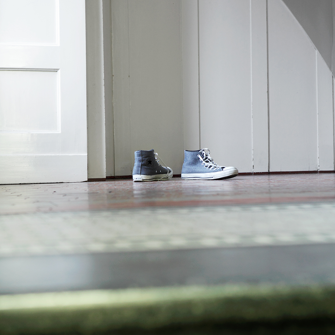 Dargestellt ist eine Alltagsszene oder Stillleben. Hellblaue Turnschuhe stehen in einer Wohnung vor einer weißen, geschlossenen Zimmertür